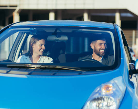Male driving instructor and female driving school student sitting together in car smiling, learning to drive a car