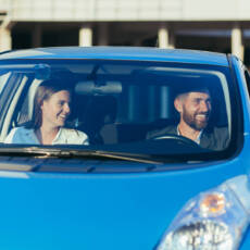 Male driving instructor and female driving school student sitting together in car smiling, learning to drive a car